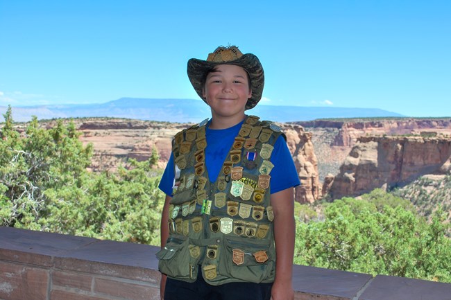 young man with vest covered in JR badges, standing in front of monument canyons
