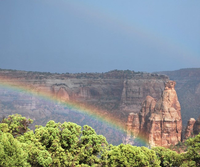 Double rainbow arcs through a canyon with monoliths in the background.