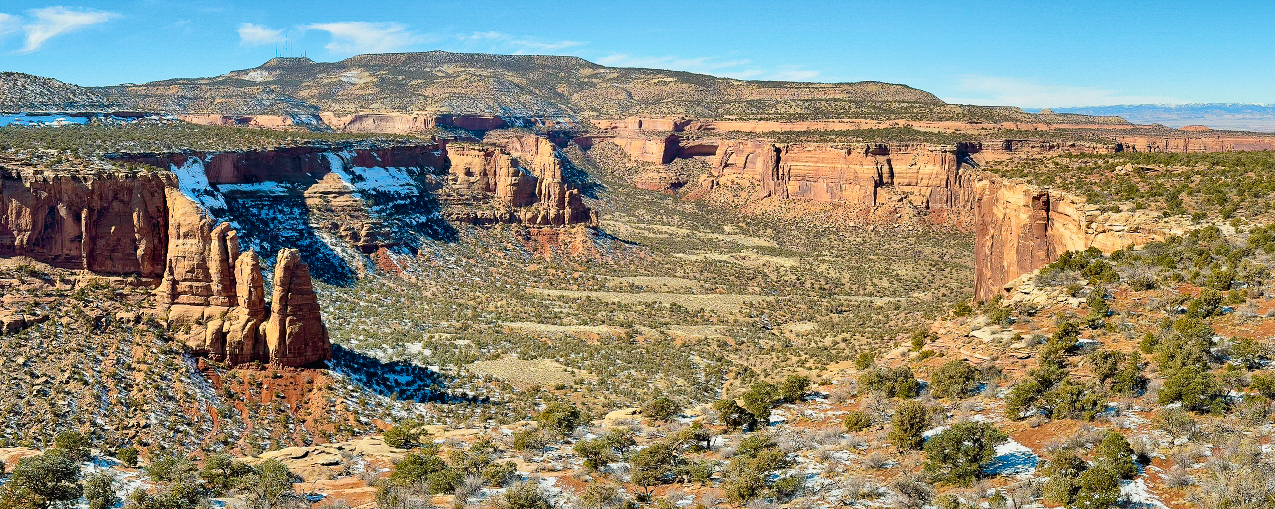wide canyon with greenery on flat bottom and vertical orange sandstone cliffs