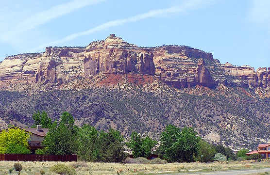 Reddish cliffs behind green broadleaf trees and roofed homes