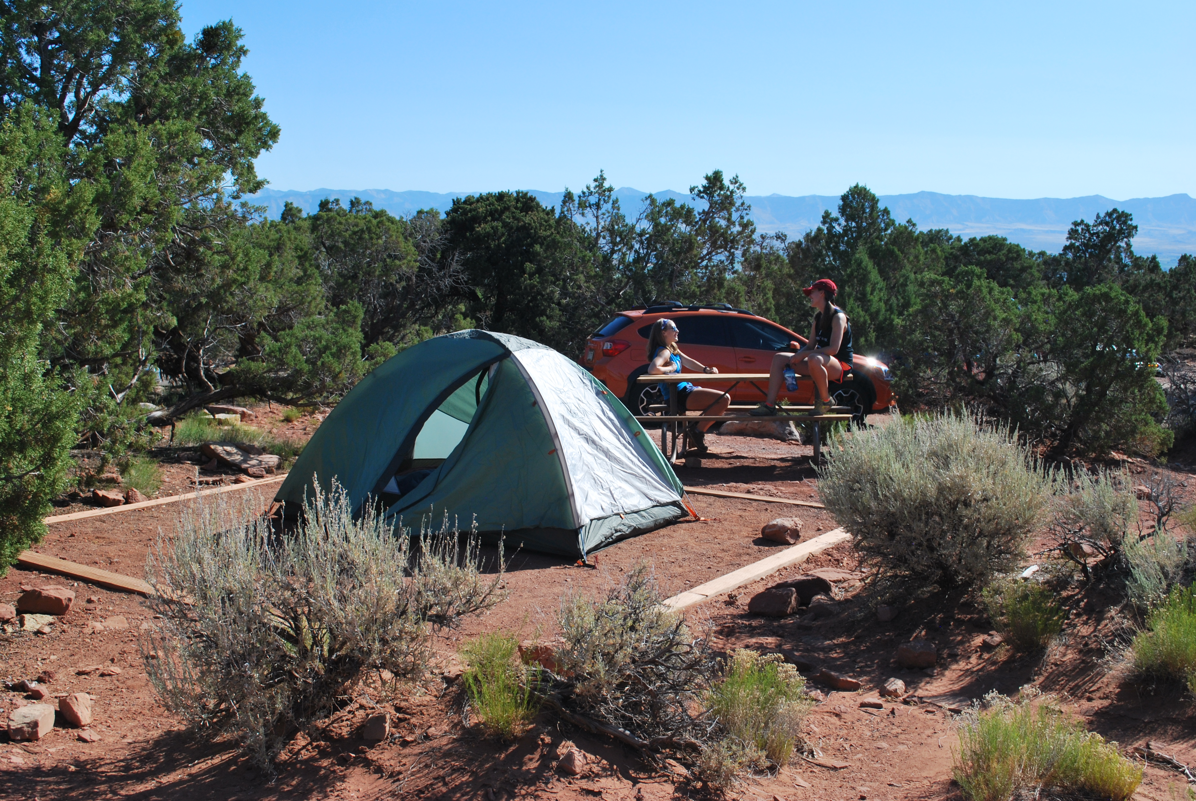 Two campers have a conversation on a picnic table behind a tent at Saddlehorn Campground. 