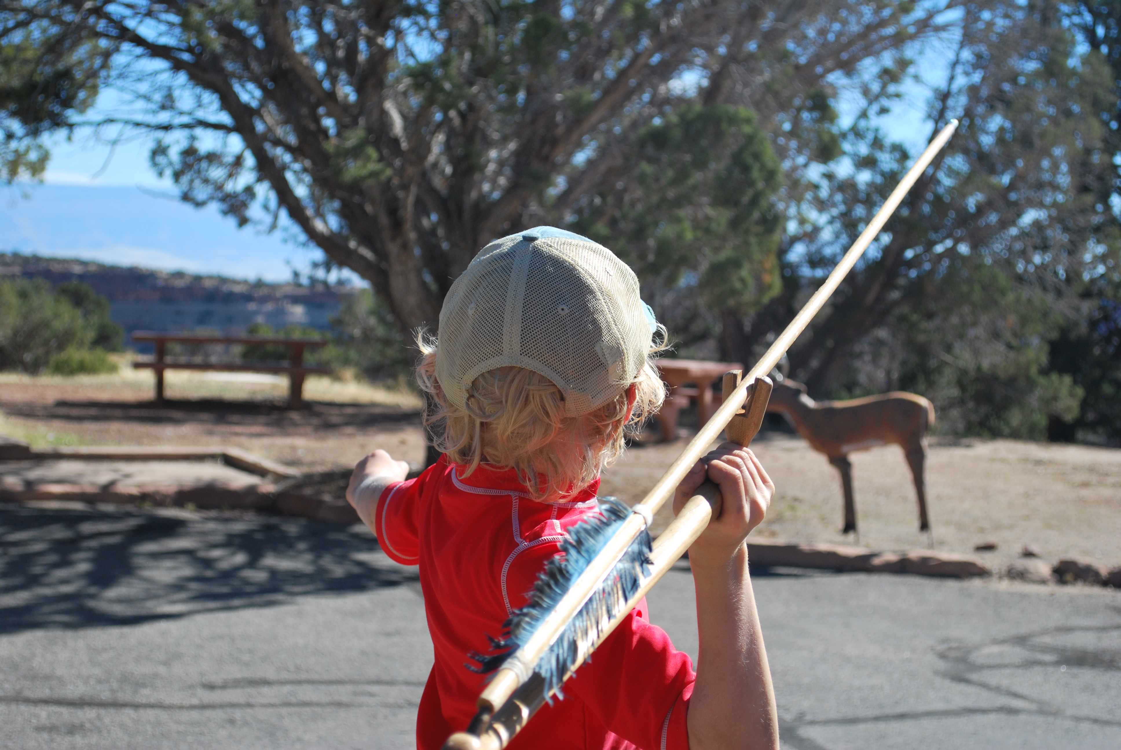 Child in red shirt and white ballcap holding an ancient spear throwing device