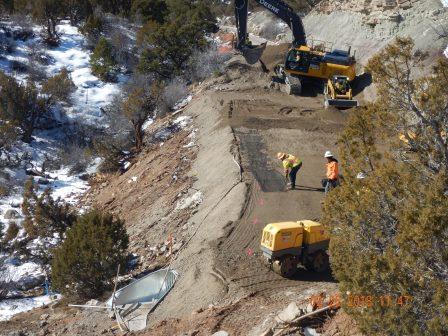 Rim Rock Drive Construction Progress February 2018 Construction crew lays geo-fabric while heavy equipment operators wait to lay dirt over it. A compactor is ready to compact the new fill.