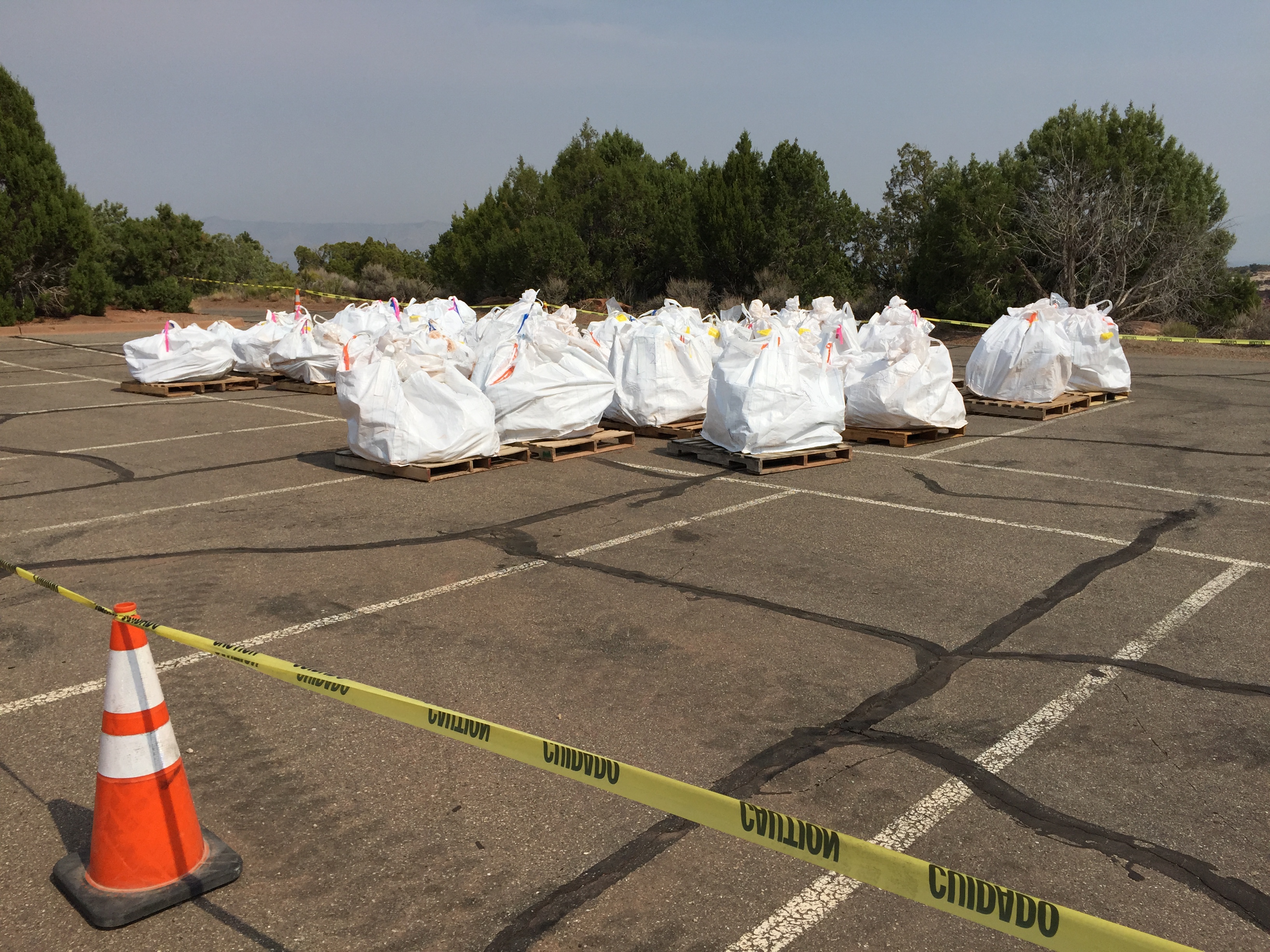 Large white bags with 1,00 pounds of rock each sitting on pallets in a parking lot.