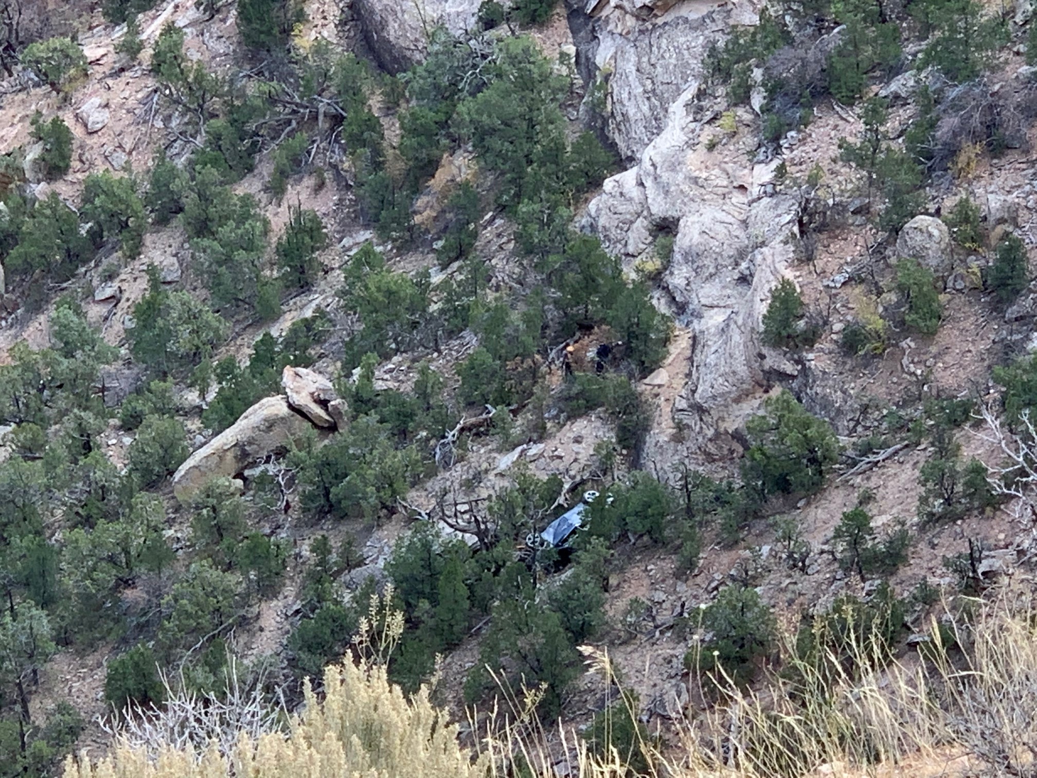 Mangled vehicle laying on side at bottom of canyon.