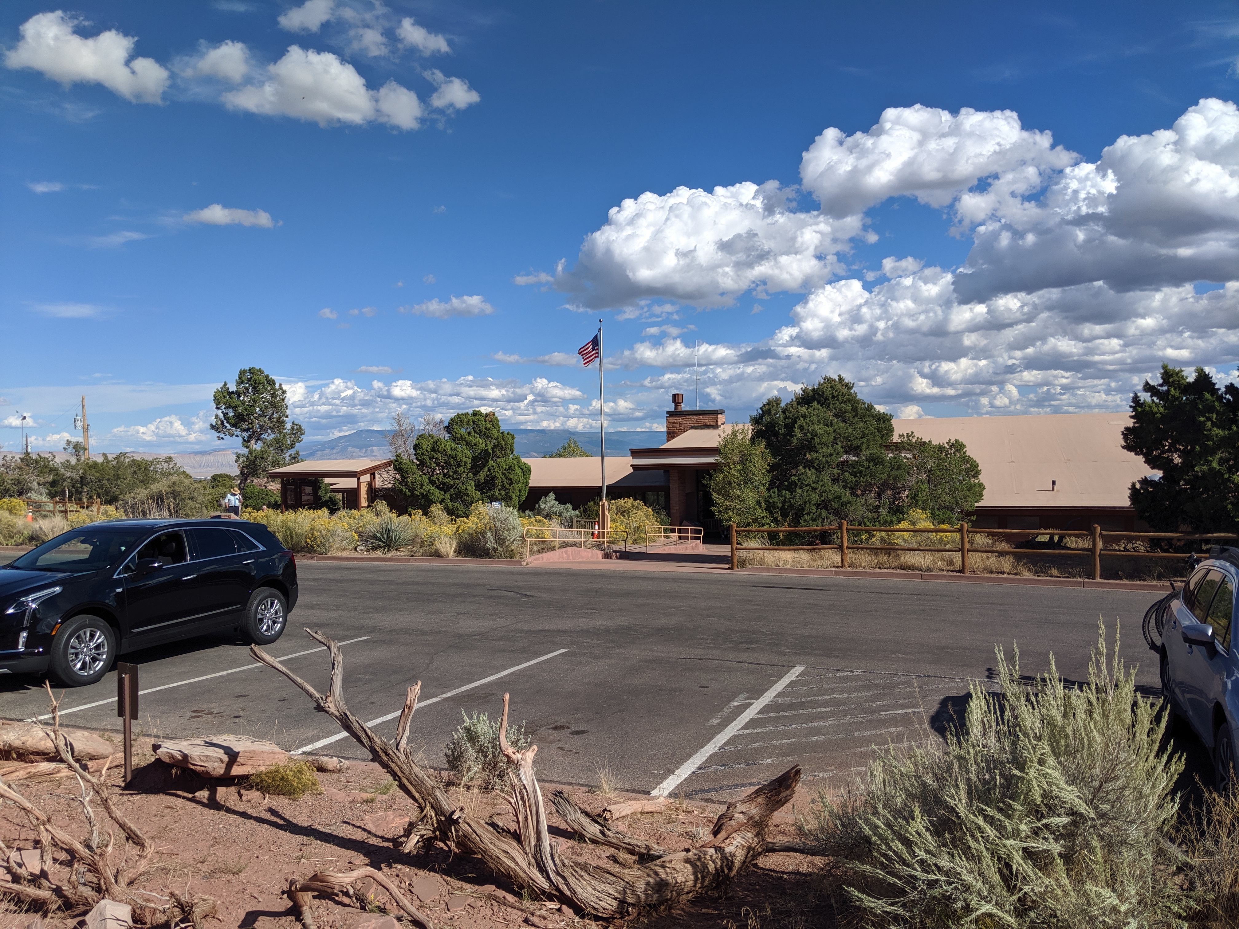 Saddlehorn Visitor Center Low building with wide tan roof, American flag flying on pole in front. Parking spaces in foreground.lot.