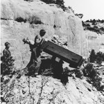 Grayscale photo of men with a wooden cart, moving stone to build Rim Rock Drive