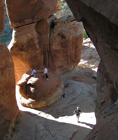 Three people look like miniatures standing within a circle of red-orange sandstone towers at Devils Kitchen
