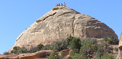 Liberty Cap, an enormous dome of gray sandstone. Several hikers stand at its highest point.