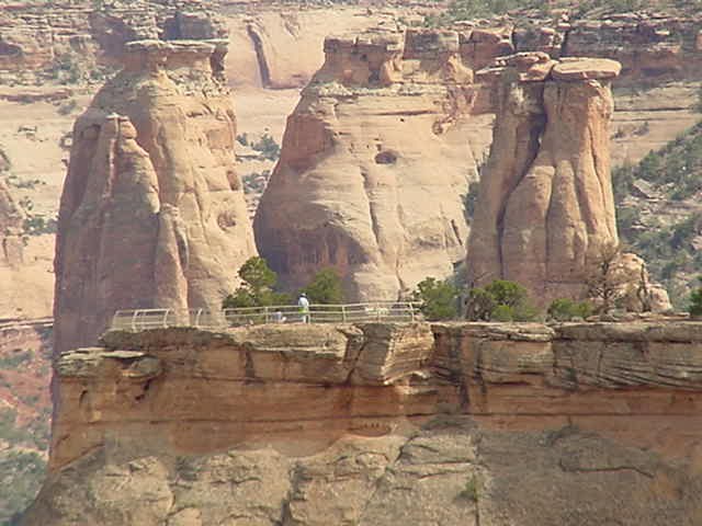 Yellow metal railings designate the overlook at the end of Otto's Trail. Behind, towers of red-orange sandstone rise from the canyon bottom.