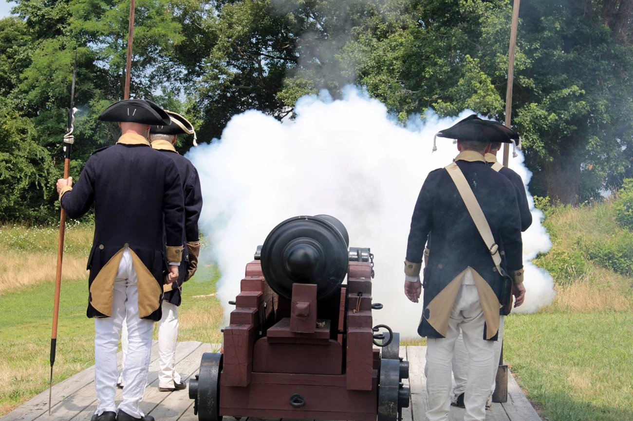Volunteers  fire an 18 pound cannon ball at Yorktown Battlefield during a Lamb's Artillery reenactment. Reenactors fire a cannon at Yorktown battlefield. They wear continental army uniforms.