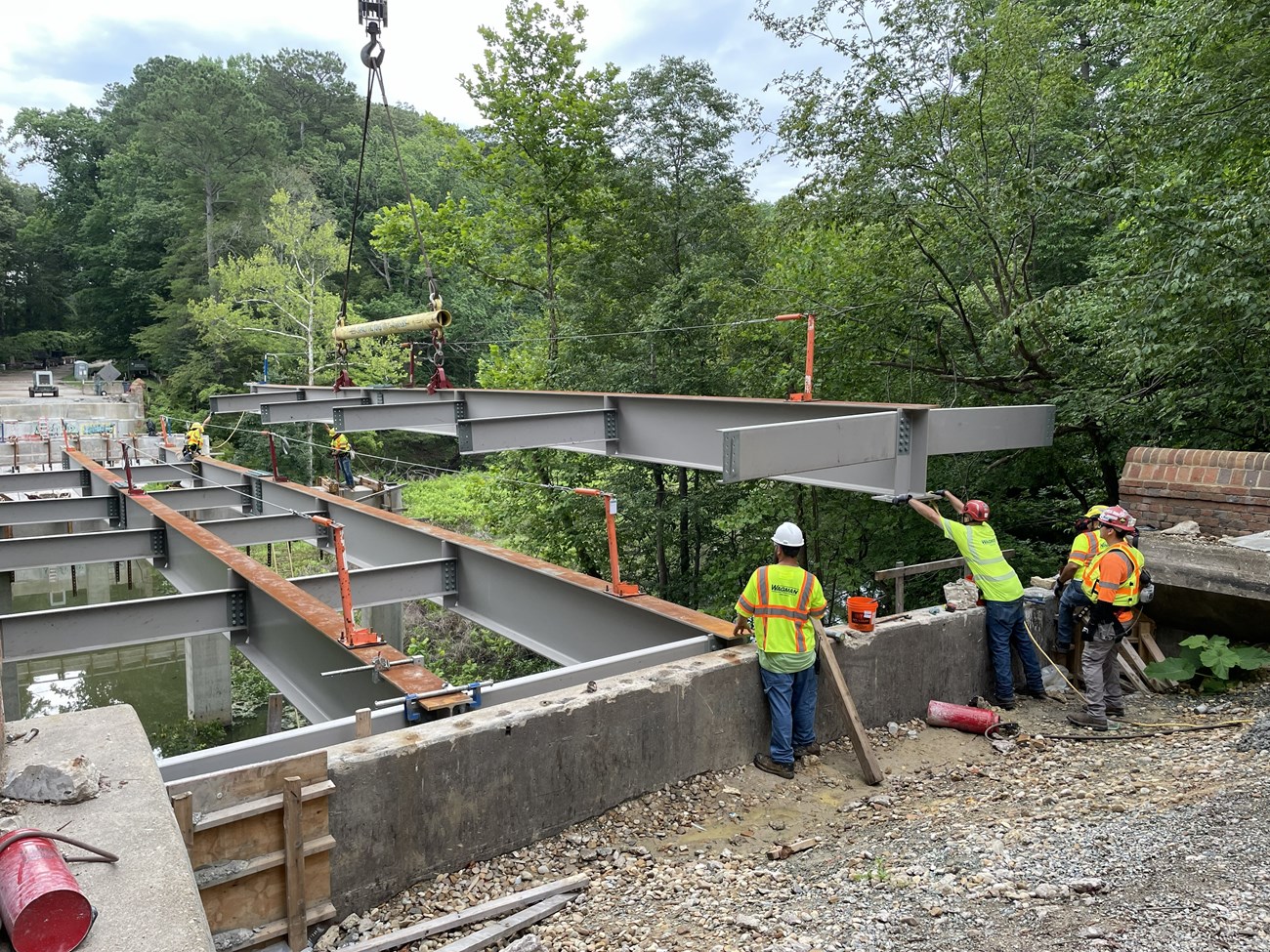 A crew of men guiding new girders onto concrete piers