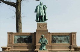 Two bronze statues of a man in a flowing coat atop one of a younger man seated. The base is brownstone with two bronze plates that are not clearly visible.