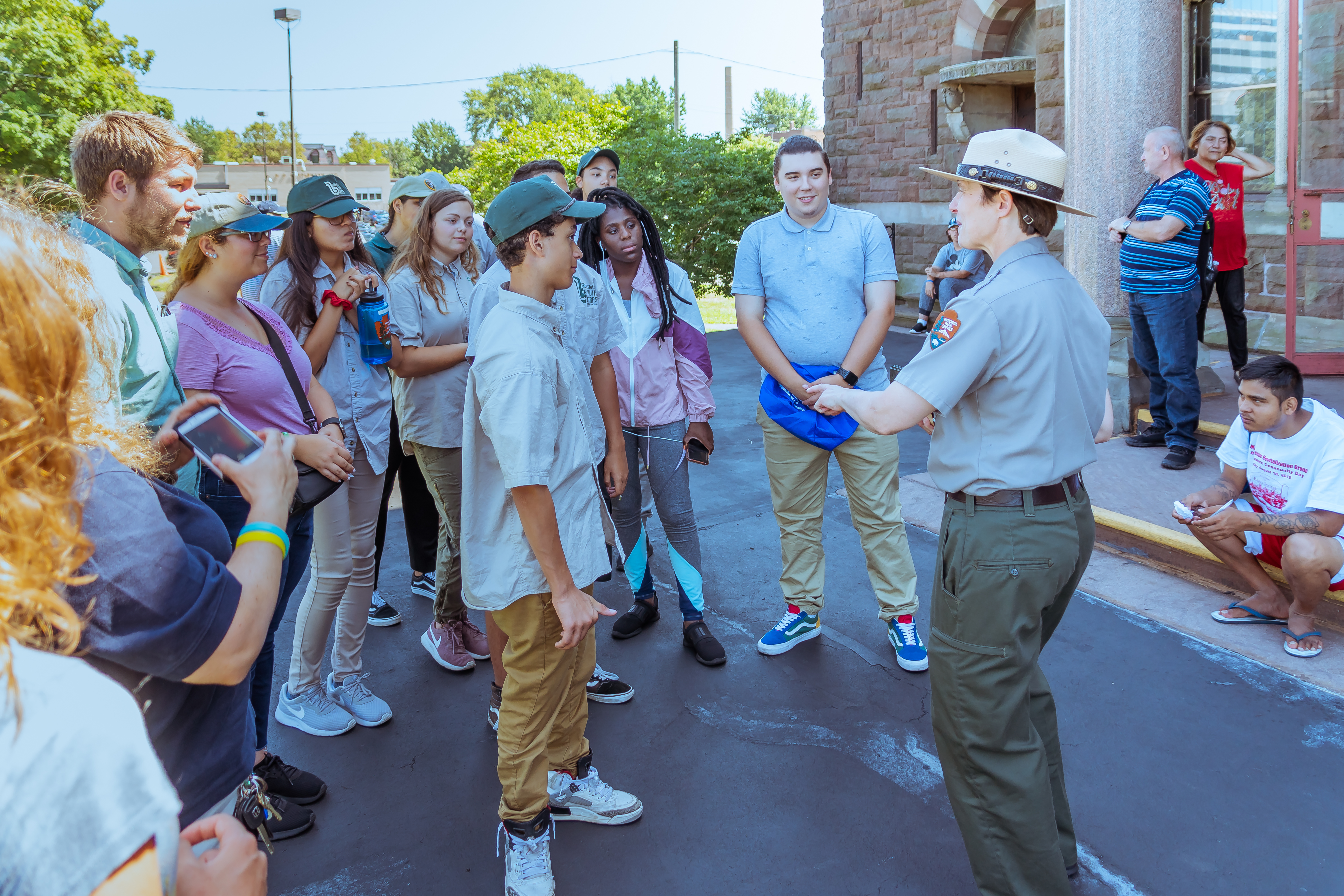 coltsville-ranger-amy-and-the-gfyc-04824_48588646767_o Park ranger in green and gray uniform with flat hat engaging with a group of young people outside a building