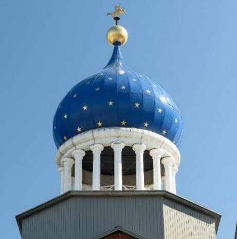 A blue onion-shaped dome with gold stars, a gold ball with a gold colt stallion statue on top all supported by white columns.