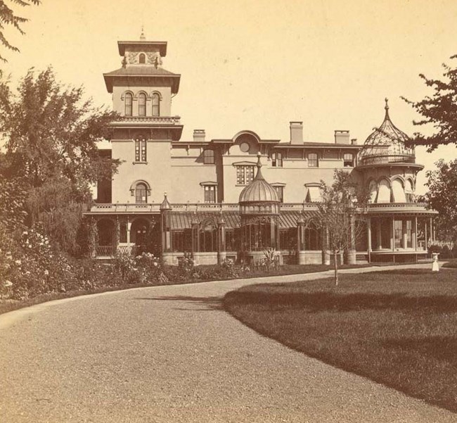 A sepia toned photo of a multistory building with windows and balconies, set behind gardens.