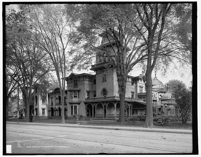 A black and white photo of a multistory building with glass domes behind a fence.