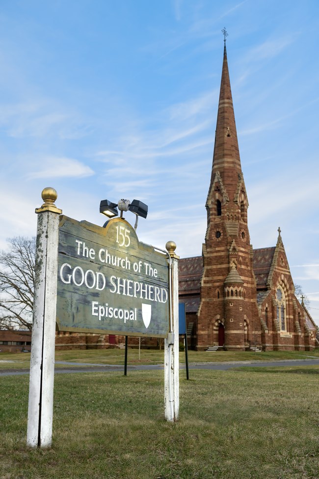 A multicolored stone church with steeple behind a church sign.