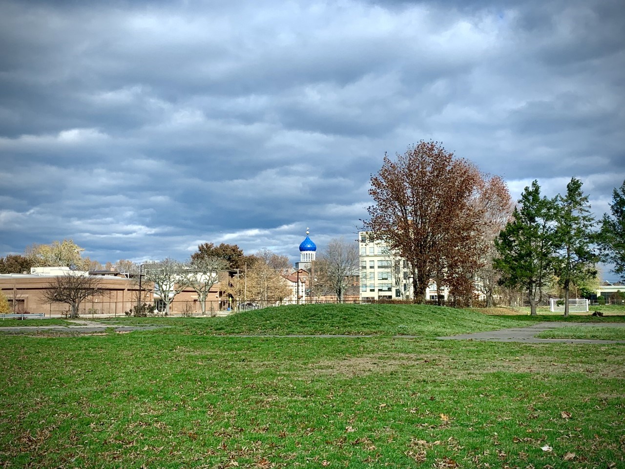A group of buildings seen from a park, with the blue Colt dome in the center.
