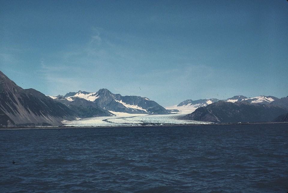 A glacier flowing between mountains down to the ocean.  There is a dark stripe running down the center of the glacier.