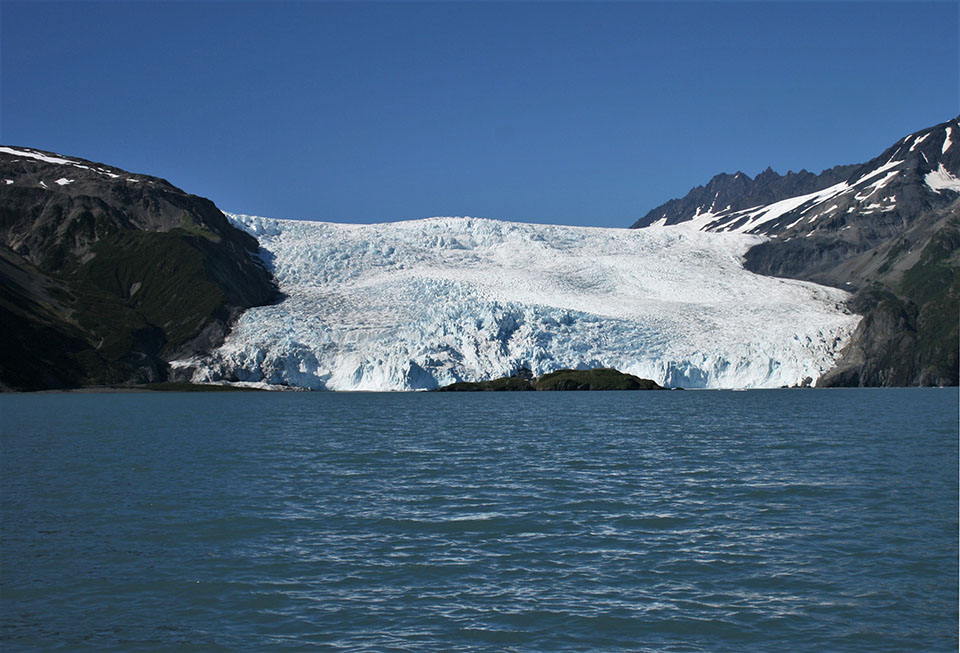 A tidewater in 1990. The glacier is in the center of the image.  The bottom of the glacier is at the edge of water.  the glacier is between two mountainsides
