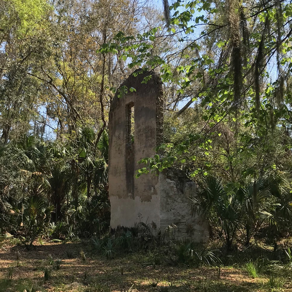 two story tabby wall in the woods with a second story window hole and worn walls on the first floor section, two men stand to the side