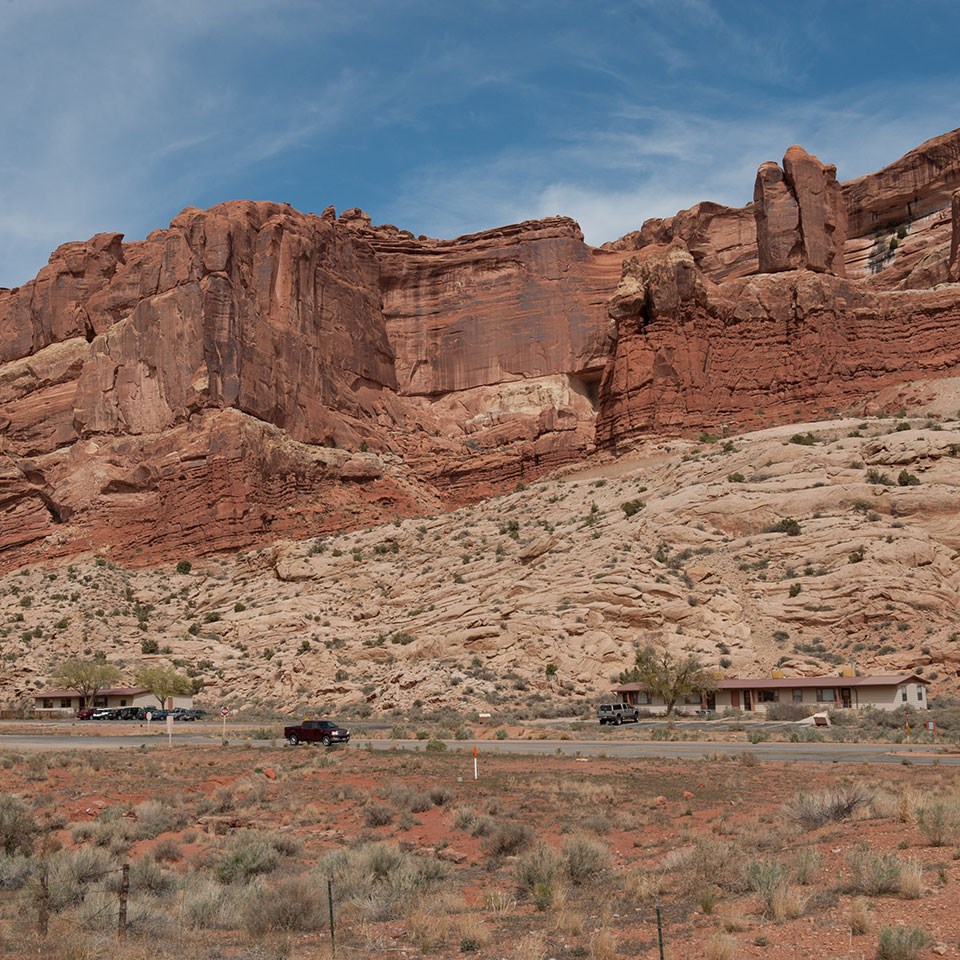 A black and white photo shows a sign reading "Arches National Monument" and a 1950s-era car sit in front of a tall rock wall in the background