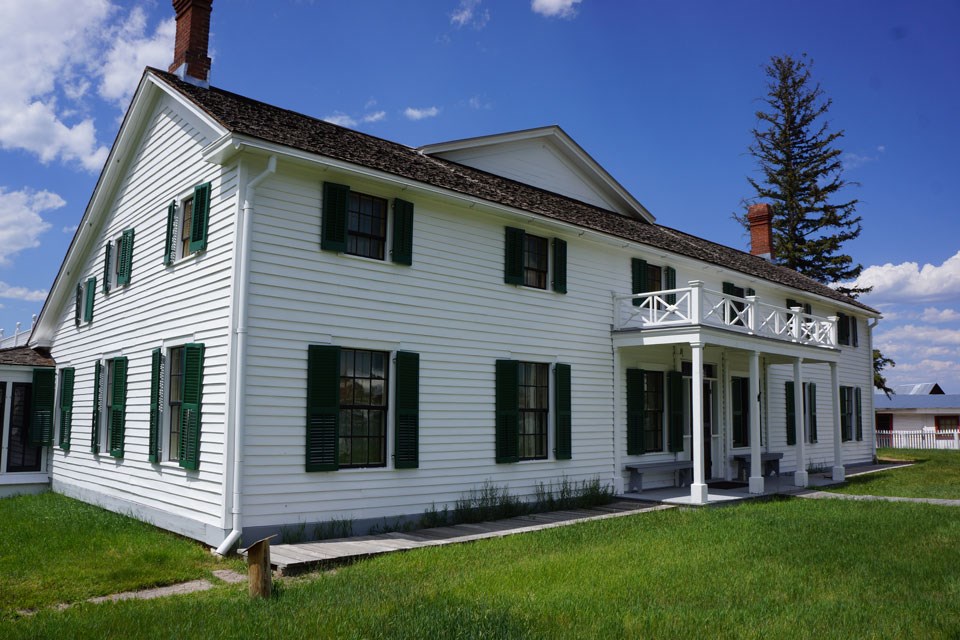 Exterior of ranch house, two story, white clapboard siding, green shutters, looking at the southeast corner.