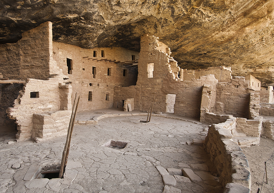 Ancient, stone-masonry village rooms under an alcove with crumbled walls and piles of rubble.