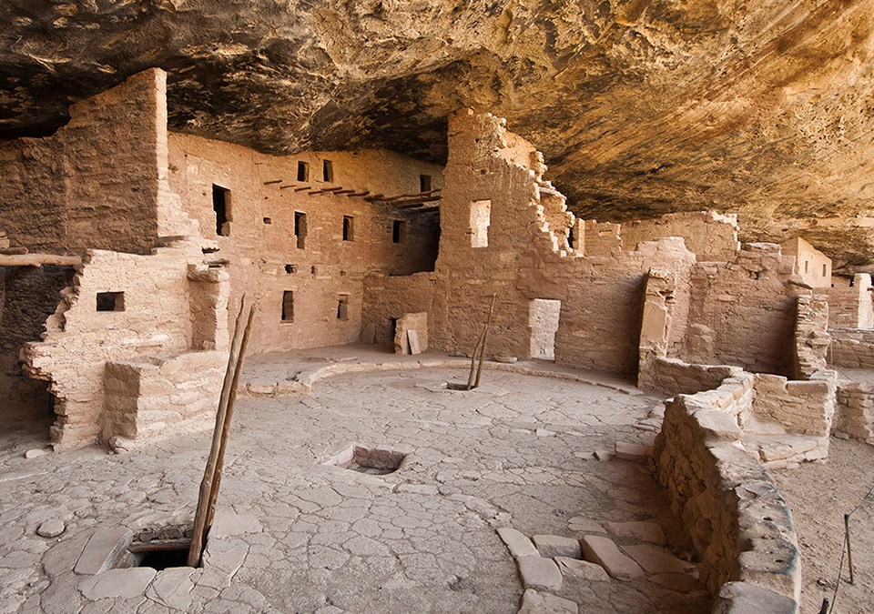 Ancient, stone-masonry village rooms under an alcove with crumbled walls and piles of rubble.