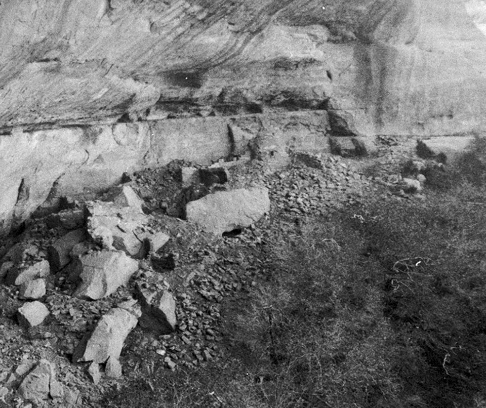 Ancient, stone-masonry village rooms under an alcove with crumbled walls and piles of rubble.