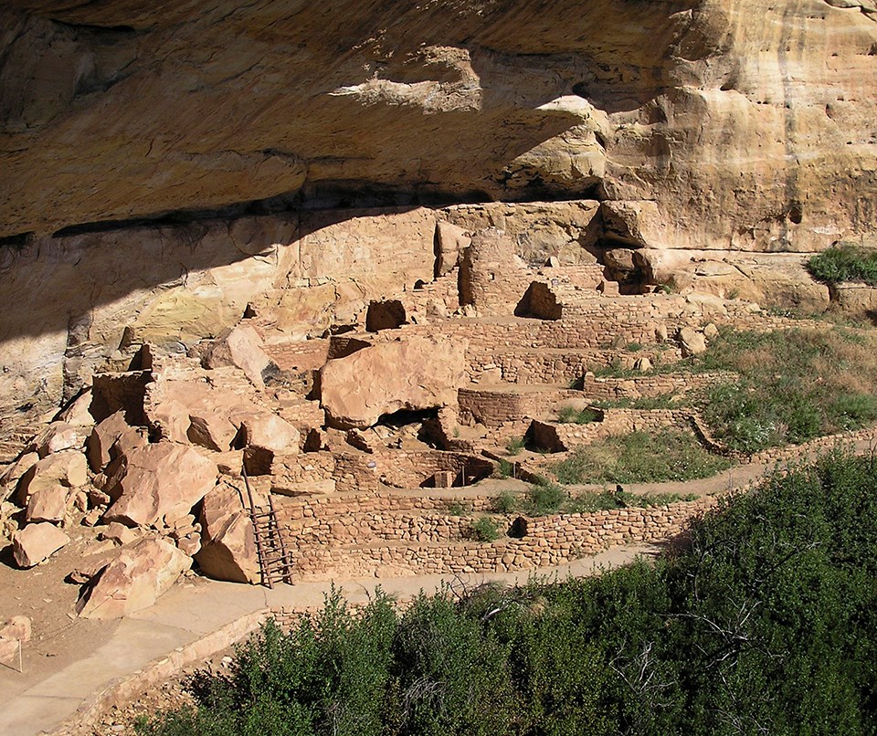 Ancient, stone-masonry village rooms under an alcove with crumbled walls and piles of rubble.