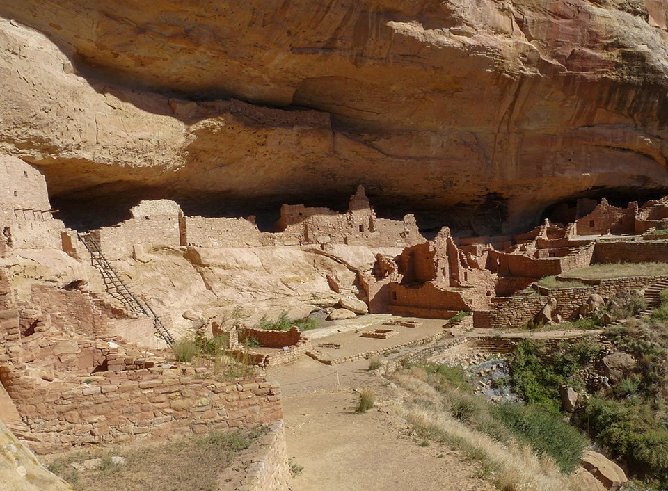 Ancient, stone-masonry village rooms under an alcove with crumbled walls and piles of rubble.