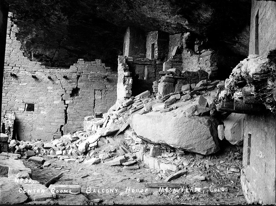 Ancient, stone-masonry village rooms under an alcove with crumbled walls and piles of rubble.