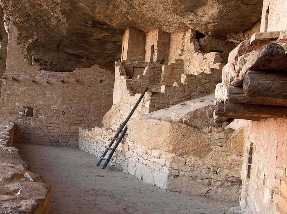 Ancient, stone-masonry village rooms under an alcove with crumbled walls and piles of rubble.