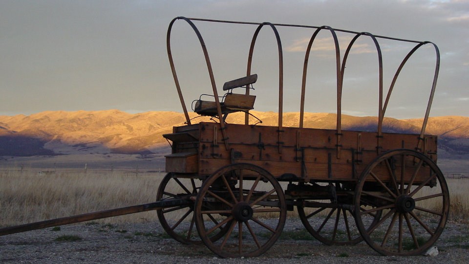 wagon box on four large wooden wheels and hooped frame on top for holding a canvas cover