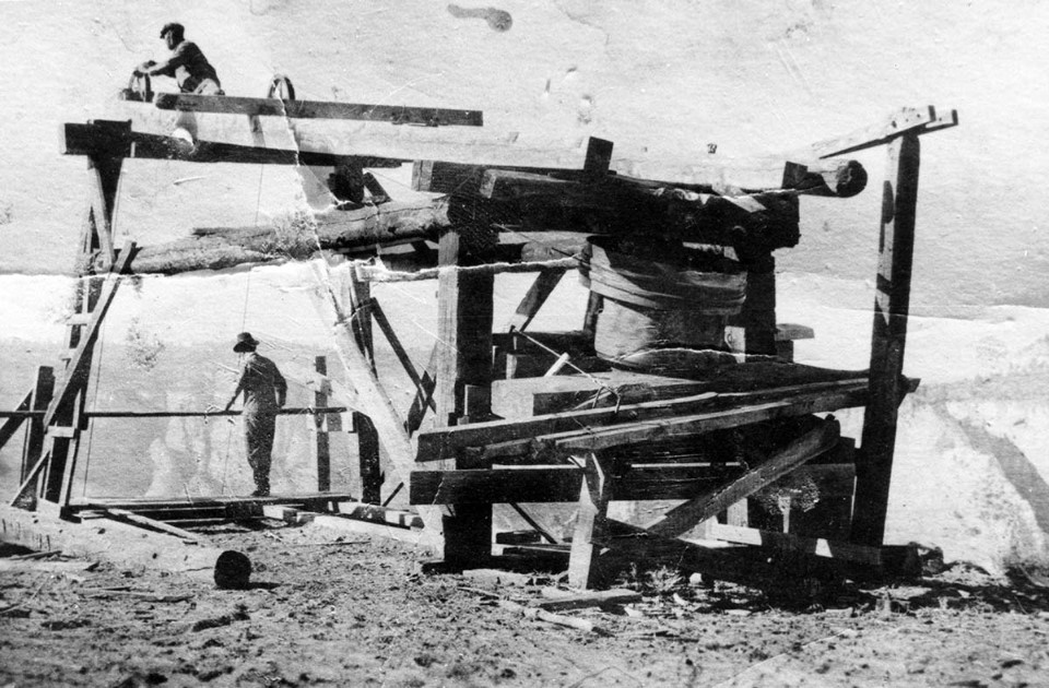 Black and white photo of a wooden structure on the rim of Zion Canyon with two men working.