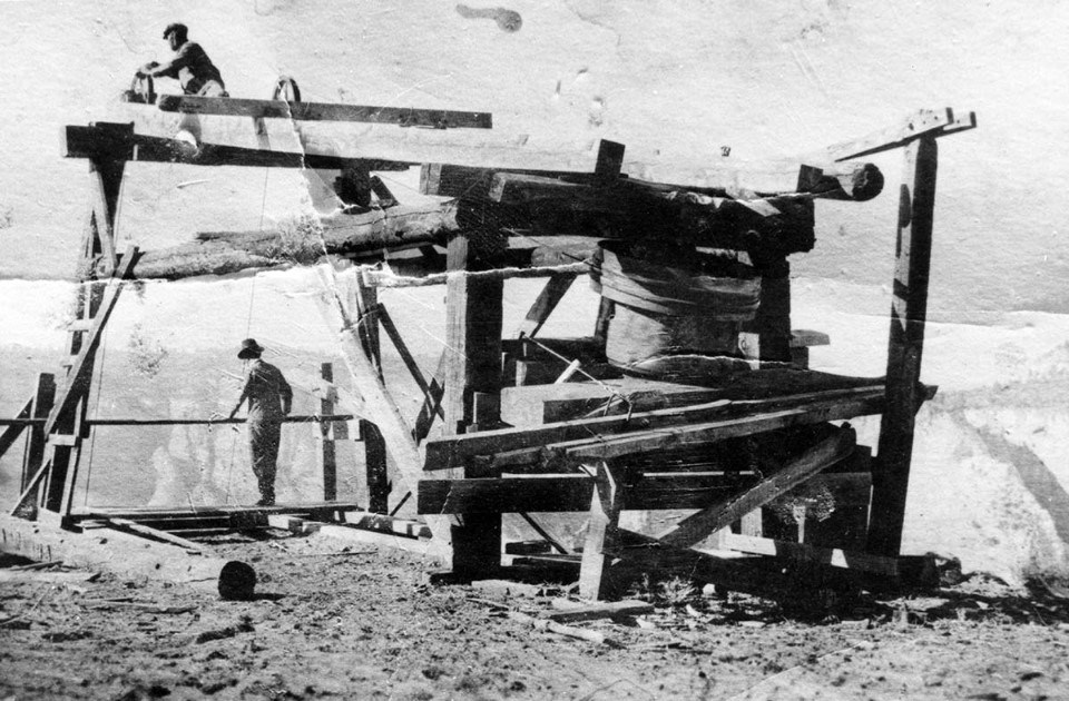 Black and white photo of a wooden structure on the rim of Zion Canyon with two men working.