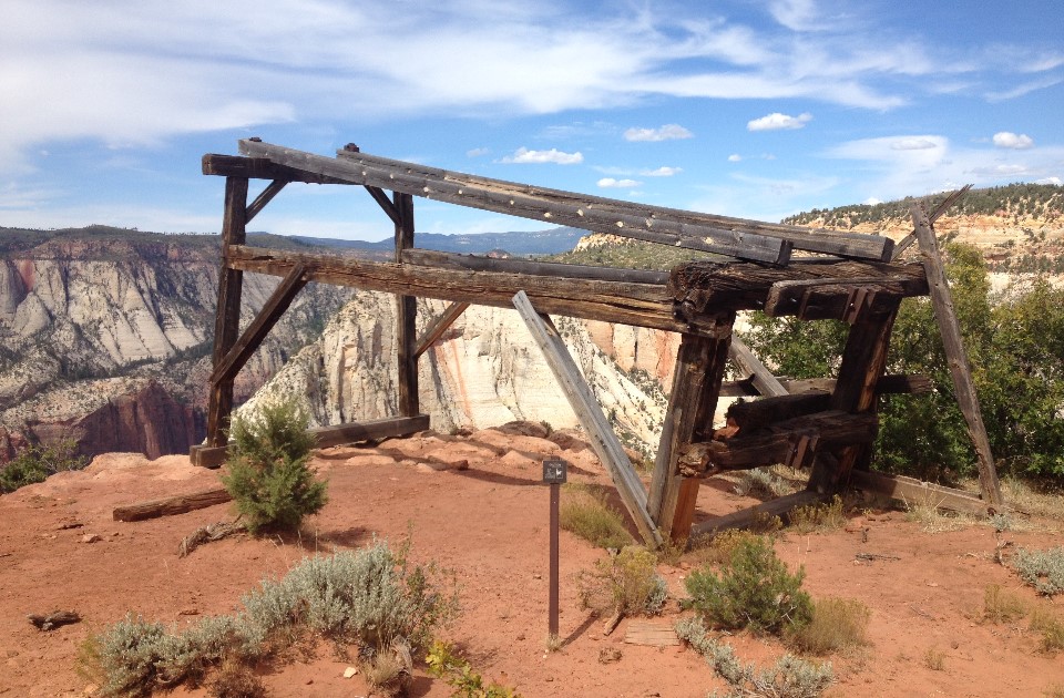 Black and white photo of a wooden structure on the rim of Zion Canyon with two men working.