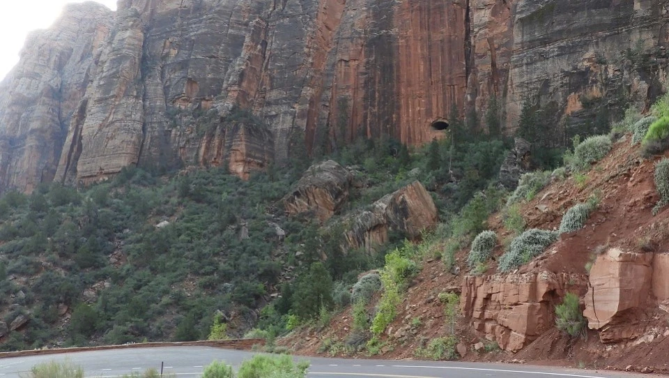 Black and white photo of men and machinery clearing a slope with a cliff in the background. A tunnel window is in the cliff.