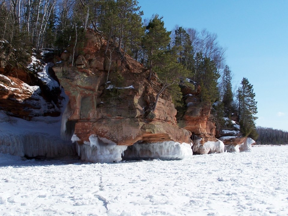 A tree-topped sandstone cliff with a frozen lake and blue sky.