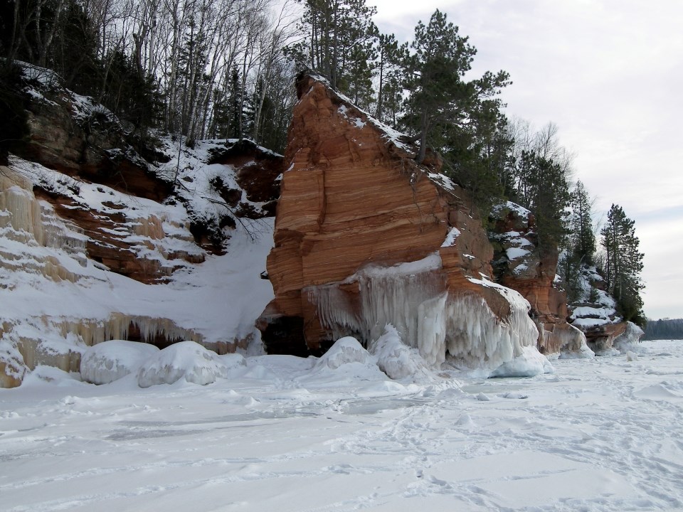 A tree-topped sandstone cliff with a frozen lake and blue sky.