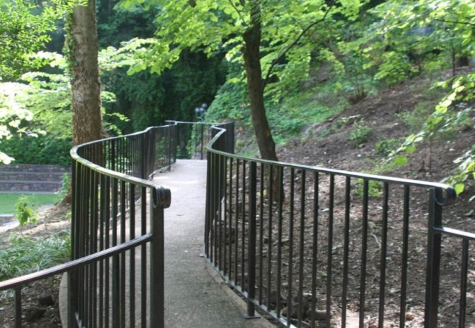 A winding trail with black railings on both sides has trees and the ground is covered with invasive species such as kudzu