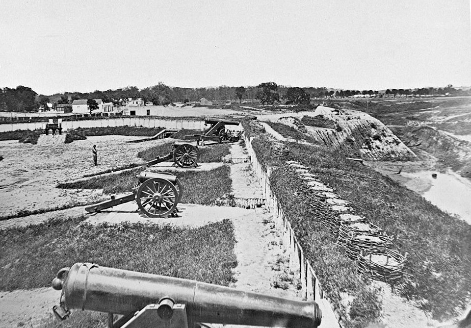Cannons lined along an embankment in a large, cleared area.