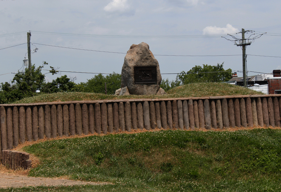 A group of men in dress coats and a seated woman in front of a stone marker