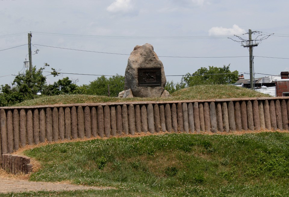 A group of men in dress coats and a seated woman in front of a stone marker