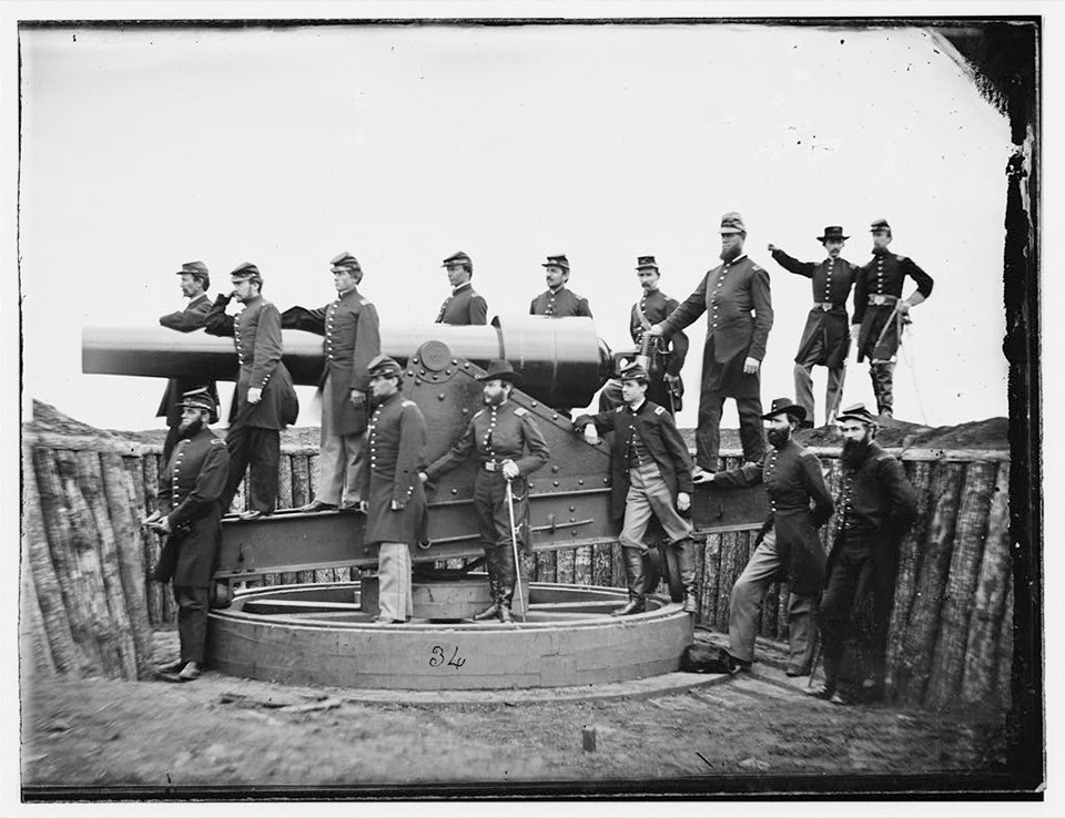 Soldiers pose with a large cannon on a fort wall