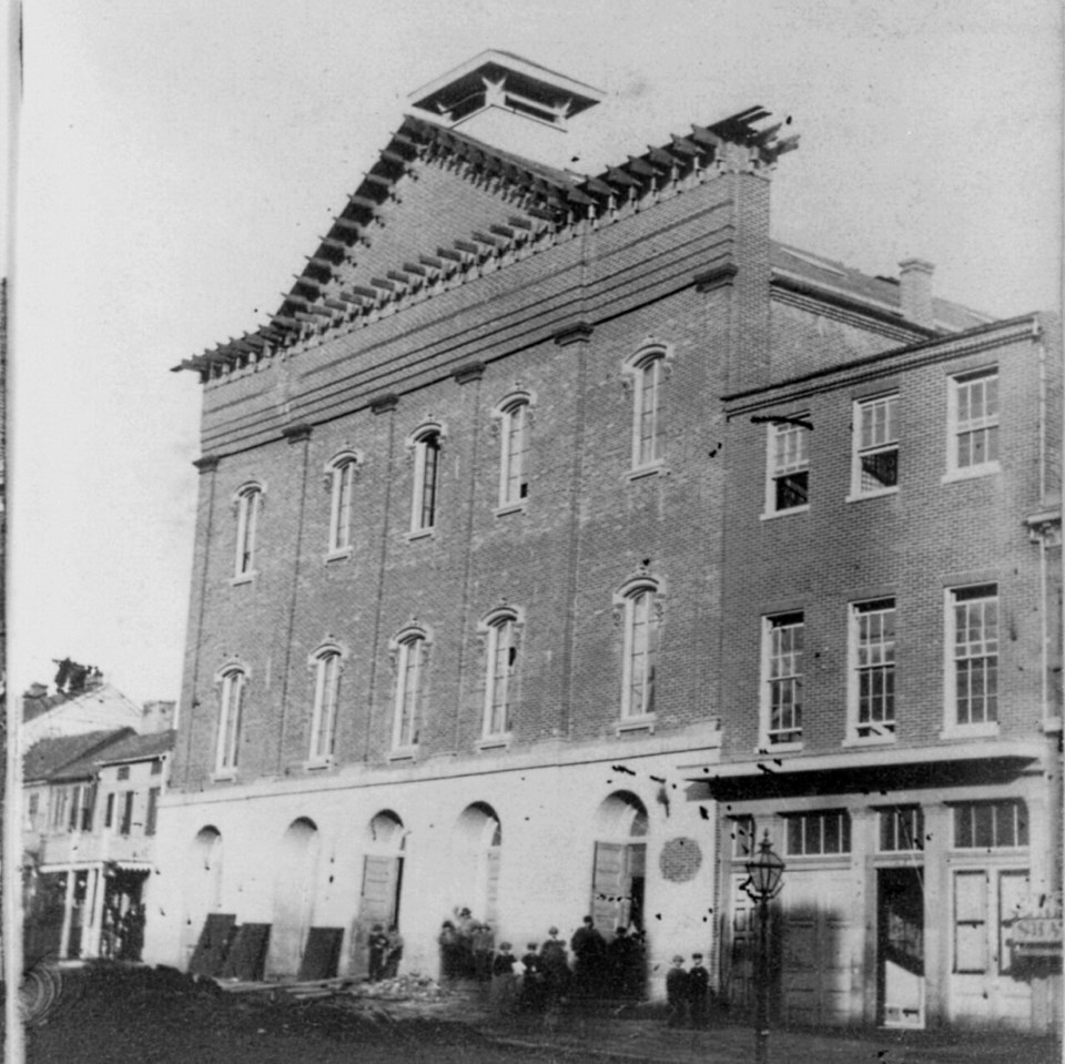 1865 Photo of Ford's Theatre with small groups of people gathered outside the front doors.