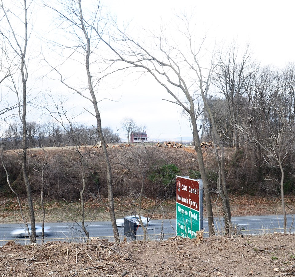 A red brick house in the distance is obscured by trees.