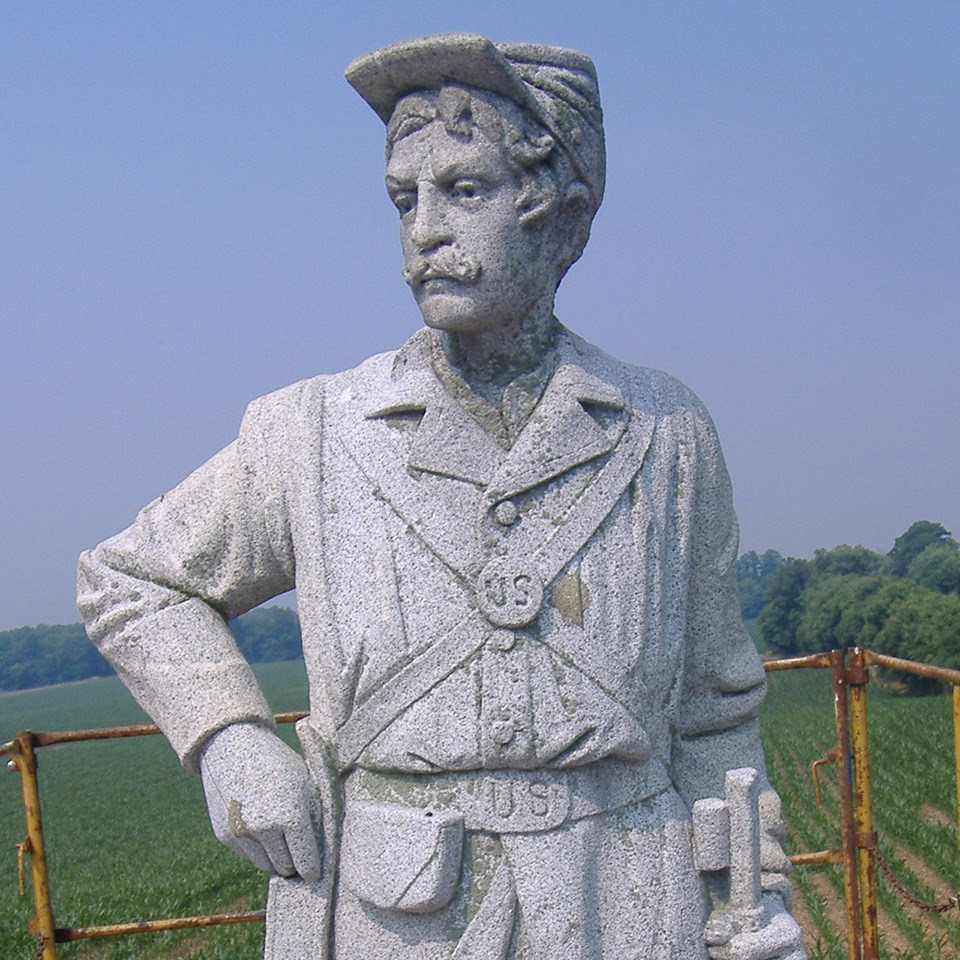 Granite statue of a Union soldier with dark specks of lichen on it. The stone appears dark gray.